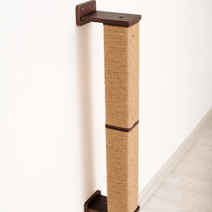May include: A wall-mounted cat scratching post. The post is rectangular, wrapped in natural-colored sisal rope, and has dark brown wooden mounting brackets at the top and bottom. The post is designed to be mounted on a wall for cats to scratch.