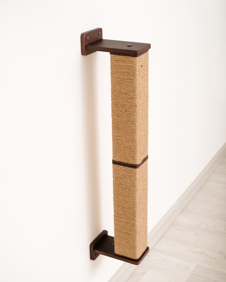May include: A wall-mounted cat scratching post. The post is rectangular, wrapped in natural-colored sisal rope, and has dark brown wooden mounting brackets at the top and bottom. The post is designed to be mounted on a wall for cats to scratch.