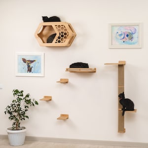 May include: A set of wall-mounted cat furniture, including a honeycomb-shaped cat house, a platform with a cat bed, and a tall scratching post with a platform. The furniture is made of wood and has a natural finish. There are three black cats in the image, one in the cat house, one on the platform, and one on the scratching post.