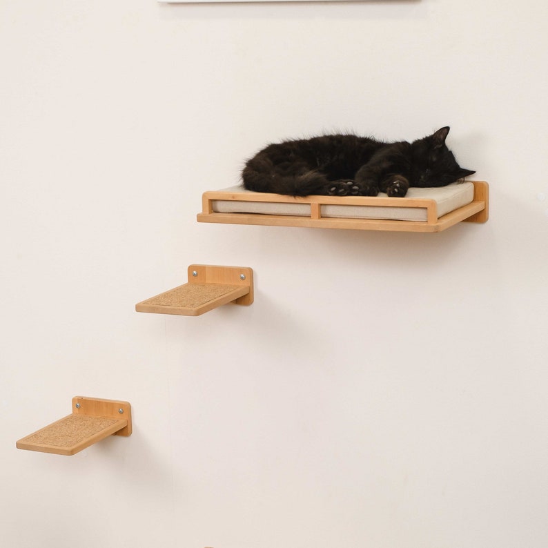 May include: A black cat sleeping on a beige cat bed mounted on a wooden shelf. Two smaller wooden shelves with scratching posts are below the cat bed.