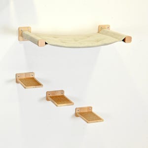 May include: A wall-mounted cat furniture set featuring a beige hammock and three wooden steps. The hammock is suspended between wooden supports, and the steps have a cork surface. The set is designed for feline climbing and lounging.