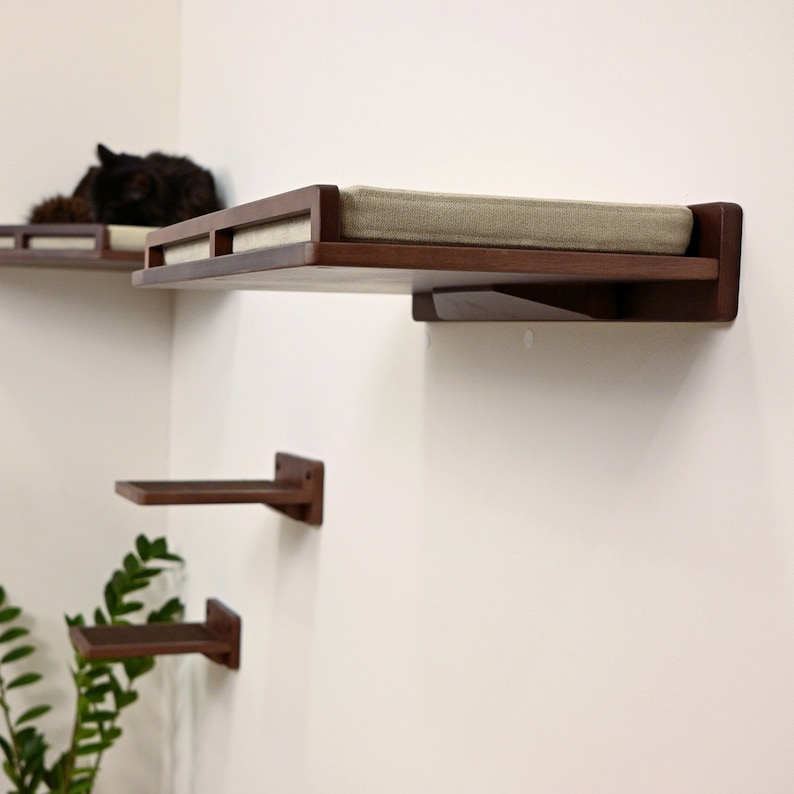 May include: A set of wall-mounted cat shelves in a modern design. The shelves are made of dark wood and feature a rectangular shape with a cushioned top. The set includes multiple shelves of varying sizes, perfect for feline climbing and lounging.