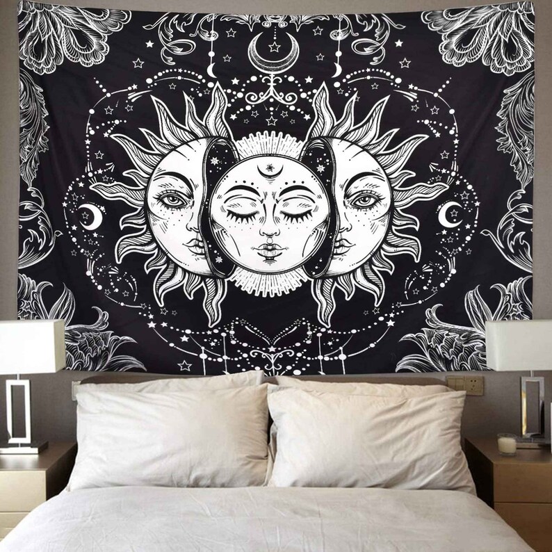 May include: Black and white tapestry featuring a sun and moon design with intricate details. The sun has a face with closed eyes and the moon has a face with open eyes. The tapestry is decorated with stars and other celestial symbols.