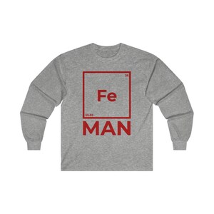 Puede incluir: Una camiseta gris de manga larga con un gr&aacute;fico cuadrado rojo que presenta el s&iacute;mbolo qu&iacute;mico "Fe" para el hierro, el n&uacute;mero at&oacute;mico "26" y el peso at&oacute;mico "55,85". El texto "MAN" est&aacute; impreso debajo del cuadrado.