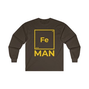 Puede incluir: Una camiseta de manga larga marr&oacute;n con un gr&aacute;fico amarillo de un elemento de la tabla peri&oacute;dica. El elemento es hierro, con el s&iacute;mbolo "Fe", el n&uacute;mero at&oacute;mico "26" y el peso at&oacute;mico "55,85". El texto "MAN" est&aacute; debajo del gr&aacute;fico del elemento.