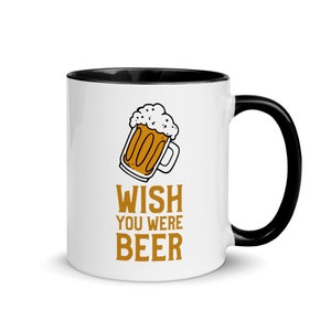 May include: White ceramic mug with a black rim and handle. The mug has a cartoon image of a beer mug with the text "WISH YOU WERE BEER" in orange.