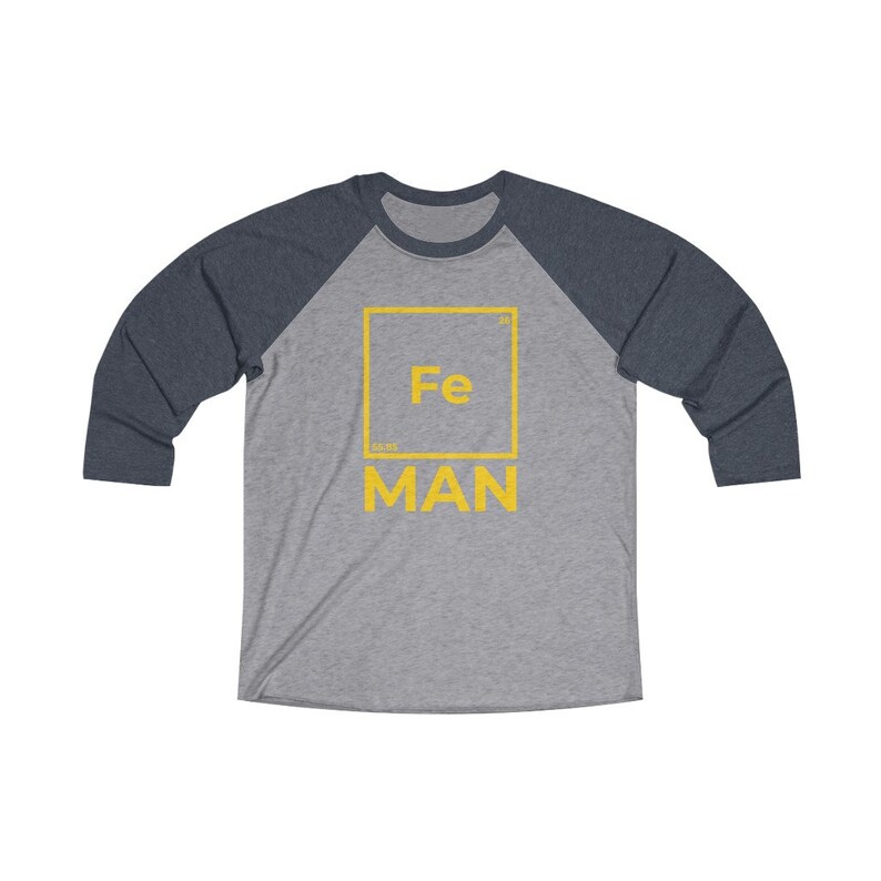 May include: A gray and navy blue baseball tee shirt with a yellow graphic of a periodic table element. The element is iron, with the symbol "Fe" and the atomic number "26". The text "MAN" is below the element symbol.