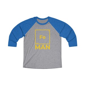 May include: A grey and blue baseball tee shirt with a yellow square graphic that says "Fe" and "MAN" underneath.
