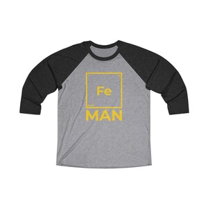 May include: A gray and black baseball tee shirt with a yellow graphic of the periodic table element iron, Fe, with the word "MAN" below it.