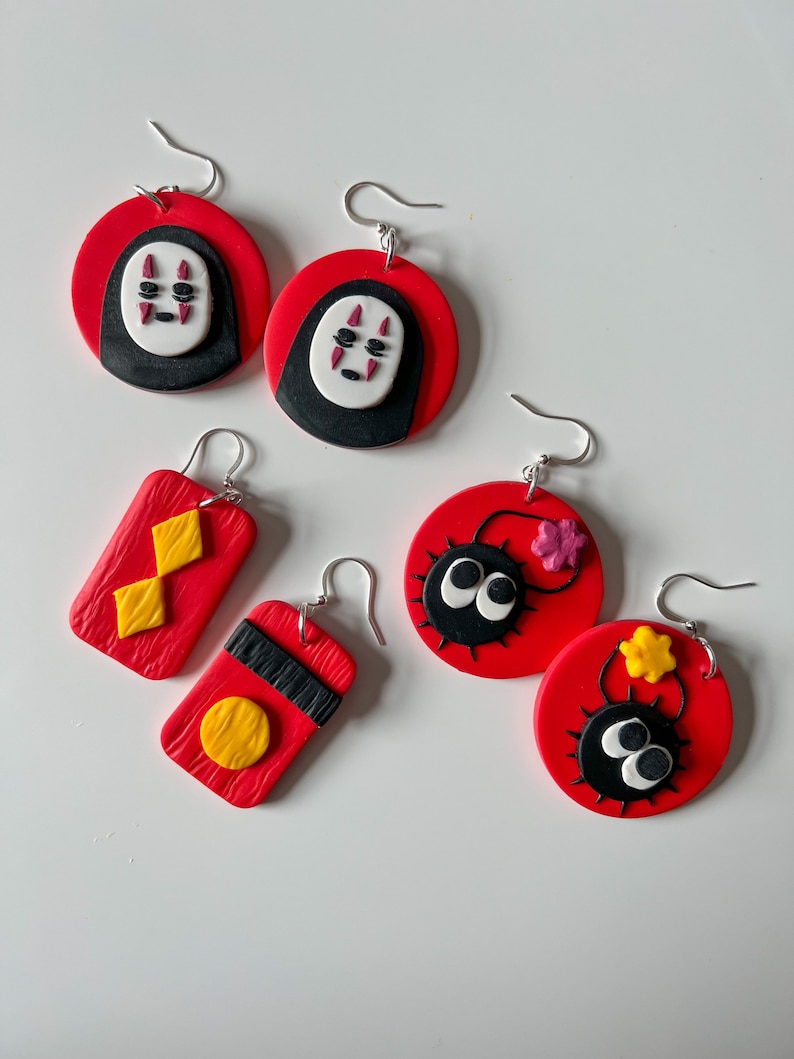 May include: A set of six red and black earrings featuring characters from the animated film Spirited Away. The earrings are made of polymer clay and feature No Face, a black and white spirit with red eyes, and a black and white bug with red eyes.