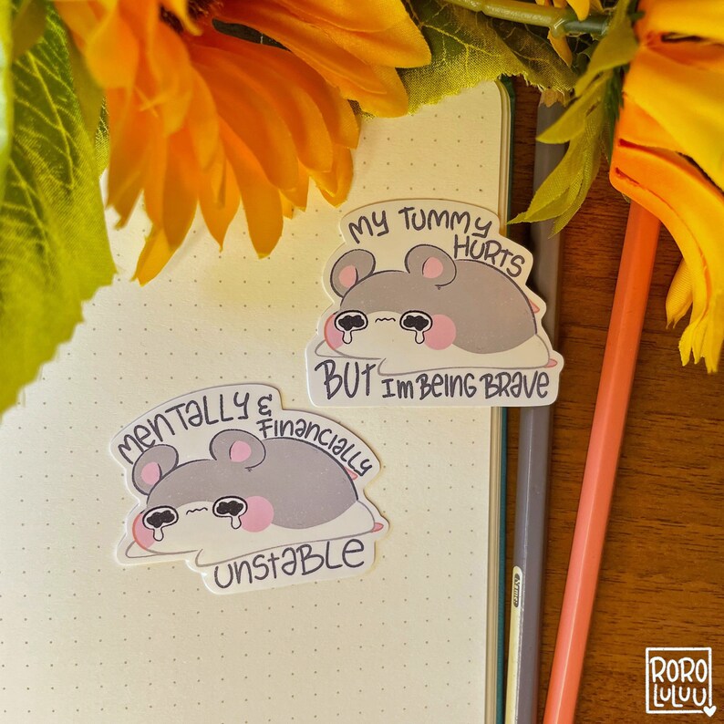 Op de afbeelding: Twee stickers met een cartoon hamster met een droevige uitdrukking. De bovenste sticker staat "Mijn buik doet pijn, maar ik ben dapper". De onderste sticker staat "Mentaal en financieel instabiel".