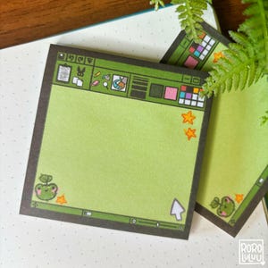 May include: Green sticky notes with a computer interface design. The notes feature a frog illustration and orange star accents. The design includes a cursor and various icons. The notes are on a white dotted surface.
