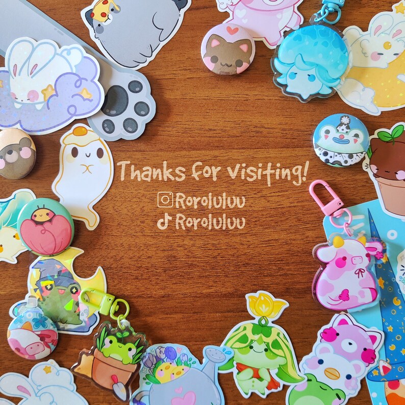 May include: A collection of colorful, cartoon-style pins and charms featuring various characters, including a ghost, a cow, a plant, and a cat. The pins are arranged in a circle around a wooden surface with the text "Thanks for visiting! @RoroLuluu  TikTok: RoroLuluu".