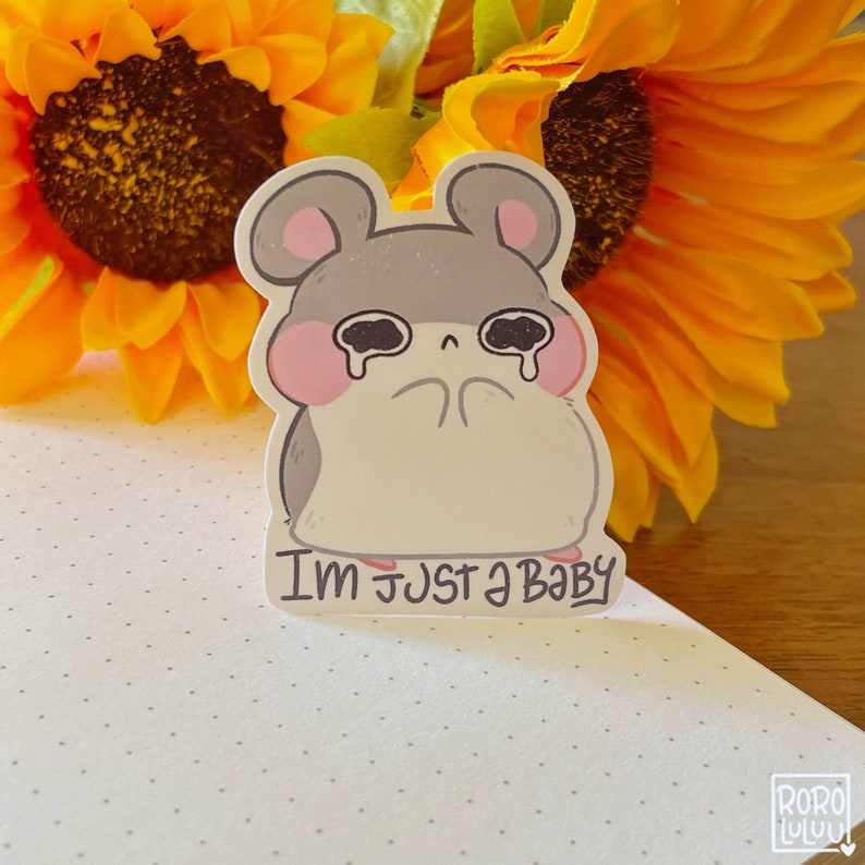 May include: A sticker featuring a cartoon hamster with big, sad eyes and the text "I'm just a baby". The hamster is gray with pink cheeks and is crying. The sticker is on a white background with a dotted pattern.