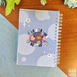 May include: A blue spiral bound sticker book with a cartoon penguin sticker on the cover. The sticker says "Sticker Book by RoroLulu" and has a heart, flower, and other small stickers on it.