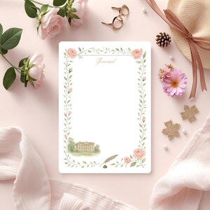 Può includere: Un diario bianco con un bordo floreale di rose rosa e foglie verdi. La parola "Journal" è scritta in alto. Un'illustrazione ad acquerello di un edificio è in basso. Il diario è circondato da fiori e accessori.