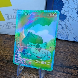 May include: A holographic Pokemon trading card featuring Bulbasaur, a green, plant-like Pokemon with a red and white Pokeball symbol. The card has the text "Bulbasaur" and "#60" in the top right corner. The card also has the text "Stun Spore" and "Tackle" with their corresponding attack values.
