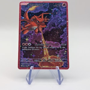 May include: A Charizard Pokémon trading card with a red border. The card features a fiery orange dragon with the text "Charizard" and "Explosive Fire". The background is a purple and black galaxy design. The card is displayed on a clear plastic stand.