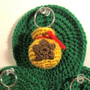 May include: Crocheted green shamrock with three brown and yellow crocheted bags hanging from it. Each bag has a red ribbon and a brown star on the front.