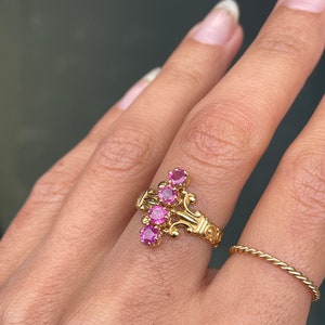 May include: A gold ring featuring a cluster of five pink gemstones set in an intricate, ornate design.