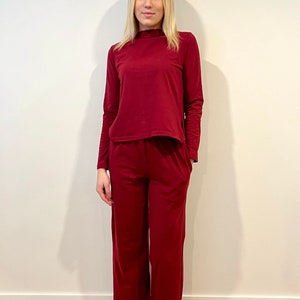 Pu&ograve; includere: Un completo da salotto bordeaux composto da due pezzi. Il set comprende un top a maniche lunghe con collo alto e pantaloni a gamba larga. L'outfit &egrave; realizzato in un materiale morbido e confortevole.