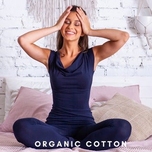 Puede incluir: Una mujer sentada en una cama con una manta de estampado rosa y blanco, lleva una blusa y pantalones de color azul marino. El texto "ORGANIC COTTON" está impreso en la manta.