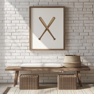 May include: A framed print featuring two crossed baseball bats in a minimalist style. The bats are a light brown color, set against a white background. The frame is a warm brown, and the artwork hangs above a wooden bench.