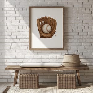May include: A framed print featuring a baseball glove and ball. The glove is brown, with a baseball nestled inside. The artwork is displayed on a white background, framed in a wooden frame. The print is hanging on a white brick wall.