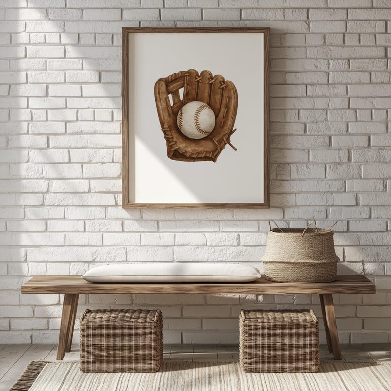 May include: A framed print featuring a baseball glove and ball. The glove is brown, with a baseball nestled inside. The artwork is displayed on a white background, framed in a wooden frame. The print is hanging on a white brick wall.