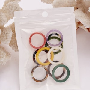 Puede incluir: Una bolsa de plástico transparente que contiene una colección de anillos coloridos. Los anillos son de varios colores, incluyendo rojo, amarillo, verde y morado. Algunos anillos tienen un efecto veteado. Los anillos están hechos de un material translúcido.