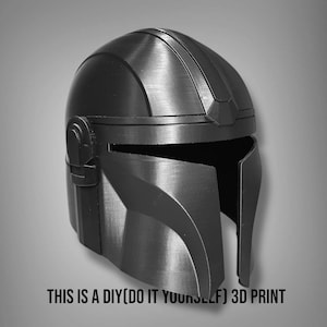 Puede incluir: Un casco mandaloriano negro y gris, una impresi&oacute;n 3D DIY. El casco tiene un acabado met&aacute;lico liso con crestas y detalles visibles. El texto en la parte inferior dice: THIS IS A DIY(DO IT YOURSELF) 3D PRINT.