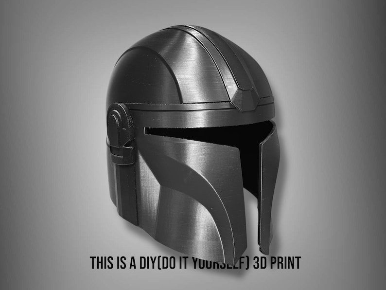 Puede incluir: Un casco mandaloriano negro y gris, una impresi&oacute;n 3D DIY. El casco tiene un acabado met&aacute;lico liso con crestas y detalles visibles. El texto en la parte inferior dice: THIS IS A DIY(DO IT YOURSELF) 3D PRINT.