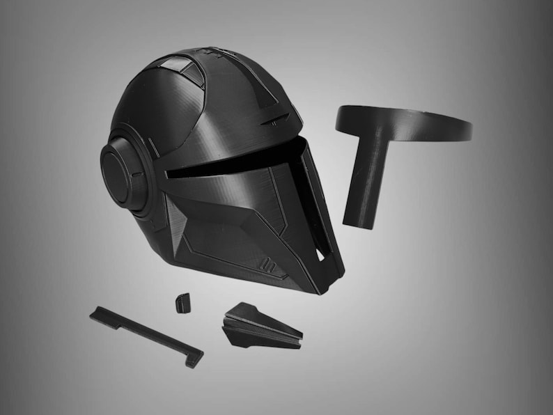 May include: A black plastic helmet with a visor and a round, circular detail on the side. The helmet is disassembled into multiple pieces, including a separate visor and a top piece.