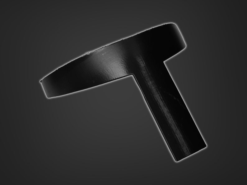 May include: A black plastic T-shaped object with a circular top. The object is designed to be used as a bottle stopper.