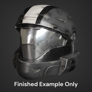 Puede incluir: Un casco negro y plateado con una franja blanca en la parte superior. El casco tiene una visera y un aspecto desgastado.