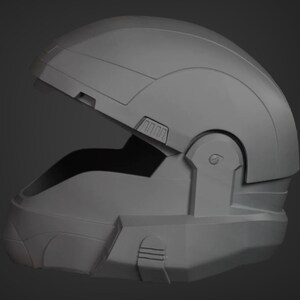 Puede incluir: Un casco gris de pl&aacute;stico con una visera parcialmente abierta. El casco tiene una superficie texturizada y un dise&ntilde;o que se asemeja a un casco de soldado futurista.