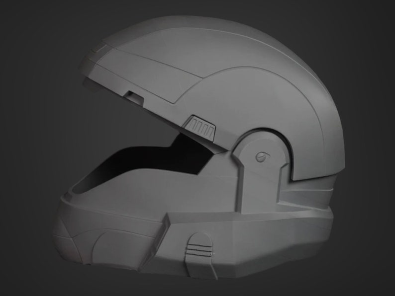 Puede incluir: Un casco gris de pl&aacute;stico con una visera parcialmente abierta. El casco tiene una superficie texturizada y un dise&ntilde;o que se asemeja a un casco de soldado futurista.