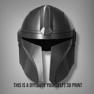Puede incluir: Un casco mandaloriano negro y gris, una impresi&oacute;n 3D DIY. El casco tiene una visera en forma de T y rasgos angulares. El texto "THIS IS A DIY(DO IT YOURSELF) 3D PRINT" est&aacute; en la parte inferior.