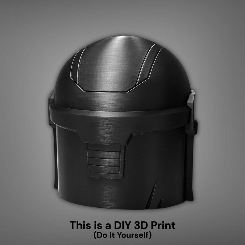 Puede incluir: Casco negro impreso en 3D con superficie texturizada. El casco tiene una parte superior redondeada con l&iacute;neas verticales y una base rectangular. El texto en la parte inferior dice: "This is a DIY 3D Print (Do It Yourself)".