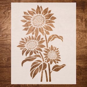 May include: A stencil featuring three stylised sunflowers with leaves. The sunflowers are in various sizes and have a detailed design.