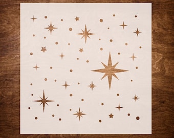 May include: A wooden stencil featuring a celestial design of stars and dots. The stars vary in size and style, with some having multiple points. The stencil is light-colored, with the star cutouts revealing the darker wood grain beneath.