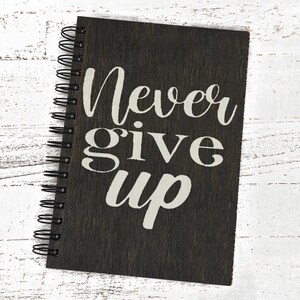 May include: A black spiral bound journal with the words "Never give up" printed in white on the front cover.