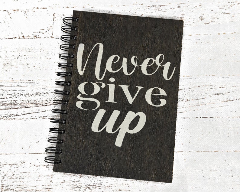 May include: A black spiral bound journal with the words "Never give up" printed in white on the front cover.