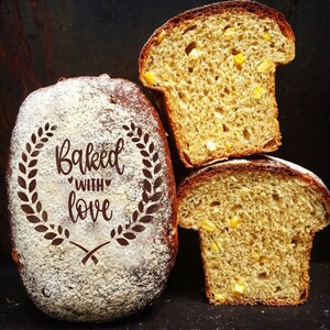 May include: Three slices of freshly baked cornbread. The loaf on the left is dusted with powdered sugar and has the words "Baked with love" written on it.