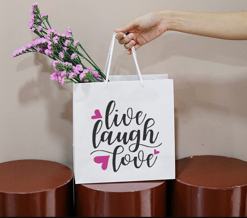 May include: White paper gift bag with pink hearts and the text "live laugh love" in black script font.