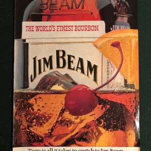 May include: An advertisement for Jim Beam bourbon. The image shows a glass of bourbon with ice, a cherry, and an orange slice. The Jim Beam logo is visible, along with the text "The World's Finest Bourbon."