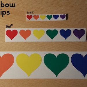 May include: Three strips of rainbow heart stickers in different sizes. The largest strip is 12 inches by 2 inches, the middle strip is 6 inches by 1 inch, and the smallest strip is 3 inches by 0.5 inches.