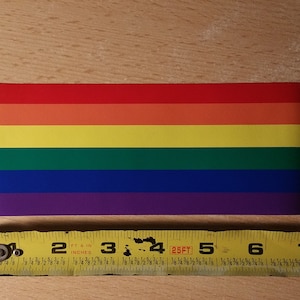 May include: A rainbow pride flag sticker measuring approximately 4 inches wide. The sticker features six horizontal stripes in the colors red, orange, yellow, green, blue, and purple.