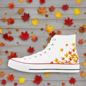 May include: White high-top canvas sneakers with a red stripe and a design of orange and brown leaves on a branch on the side.