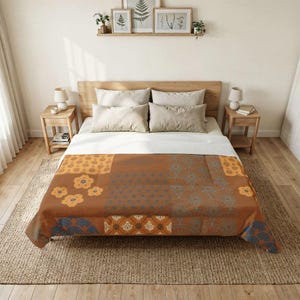 May include: A brown and orange quilt with floral and geometric patterns. The quilt features a patchwork design with various shapes and colours, including blue and yellow accents. The quilt is displayed on a bed with neutral-coloured pillows and a wooden headboard.